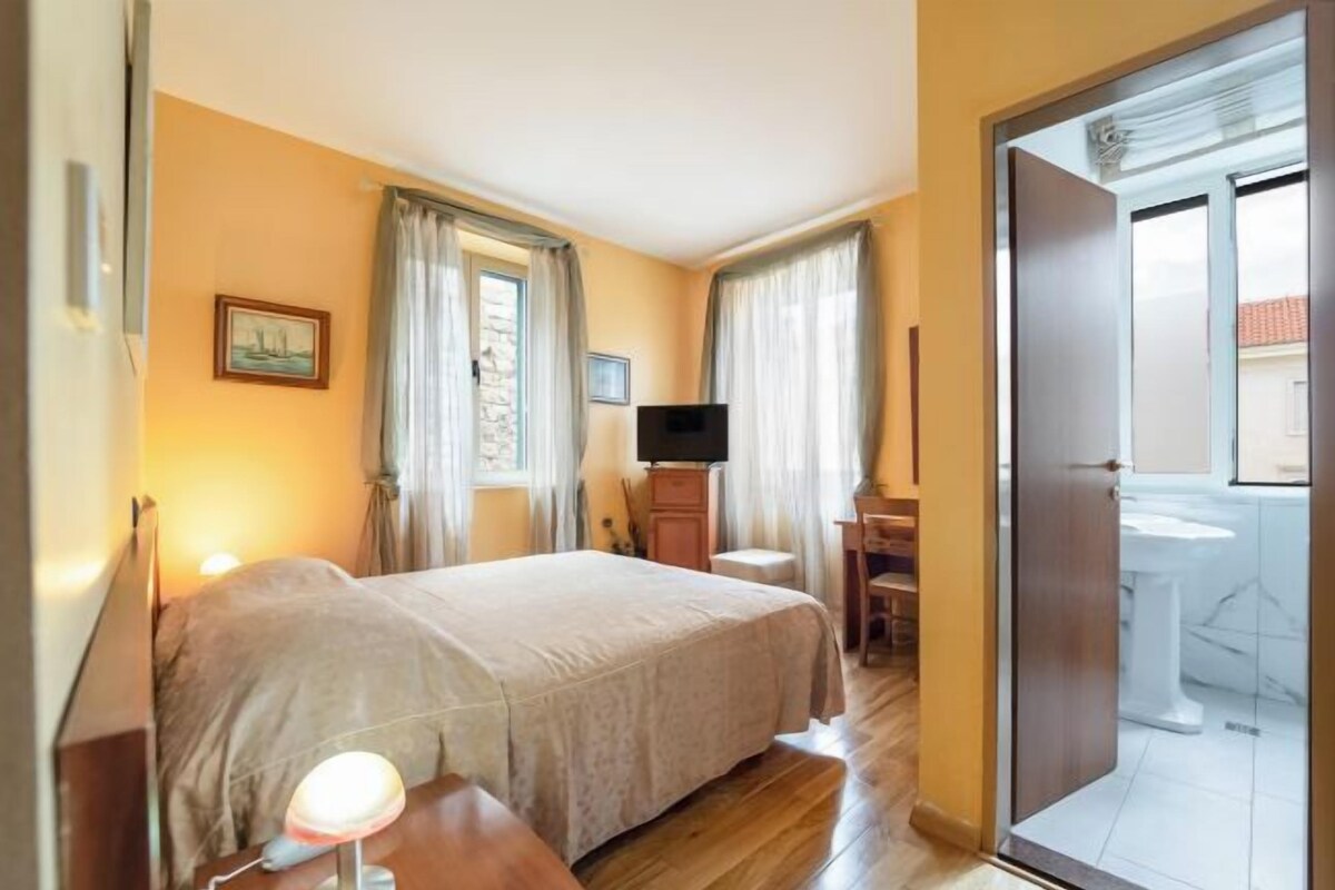 A hotel room with a bed, a desk, a television, and a bathroom visible through an open door.