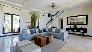 A modern living room with a sectional sofa, a wooden coffee table, and a staircase leading to another level. - Casa de Balangan by Exotiq Villa Holidays (Jimbaran)