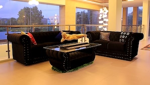 Una sala de estar moderna con dos sofás negros, una mesa de centro de vidrio y un ventanal con vista a la ciudad.