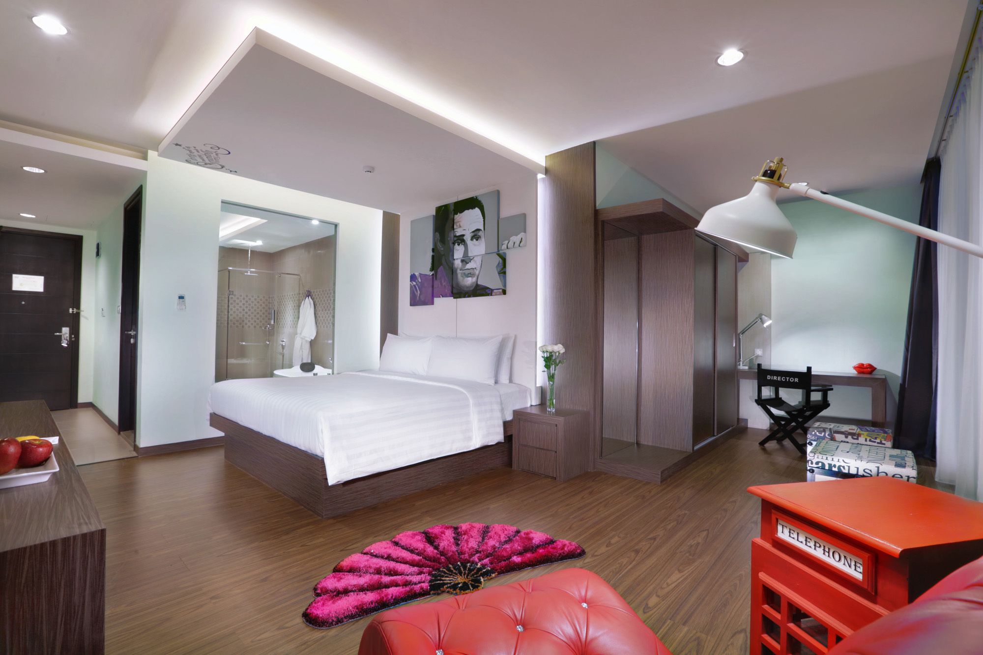 A modern hotel room with a large bed, a desk, a chair labeled "DIRECTOR", and a red telephone table.