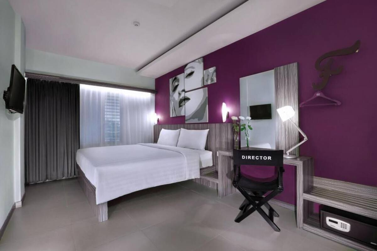 A modern hotel room with a bed, a desk with a computer, a TV, and a mirror.