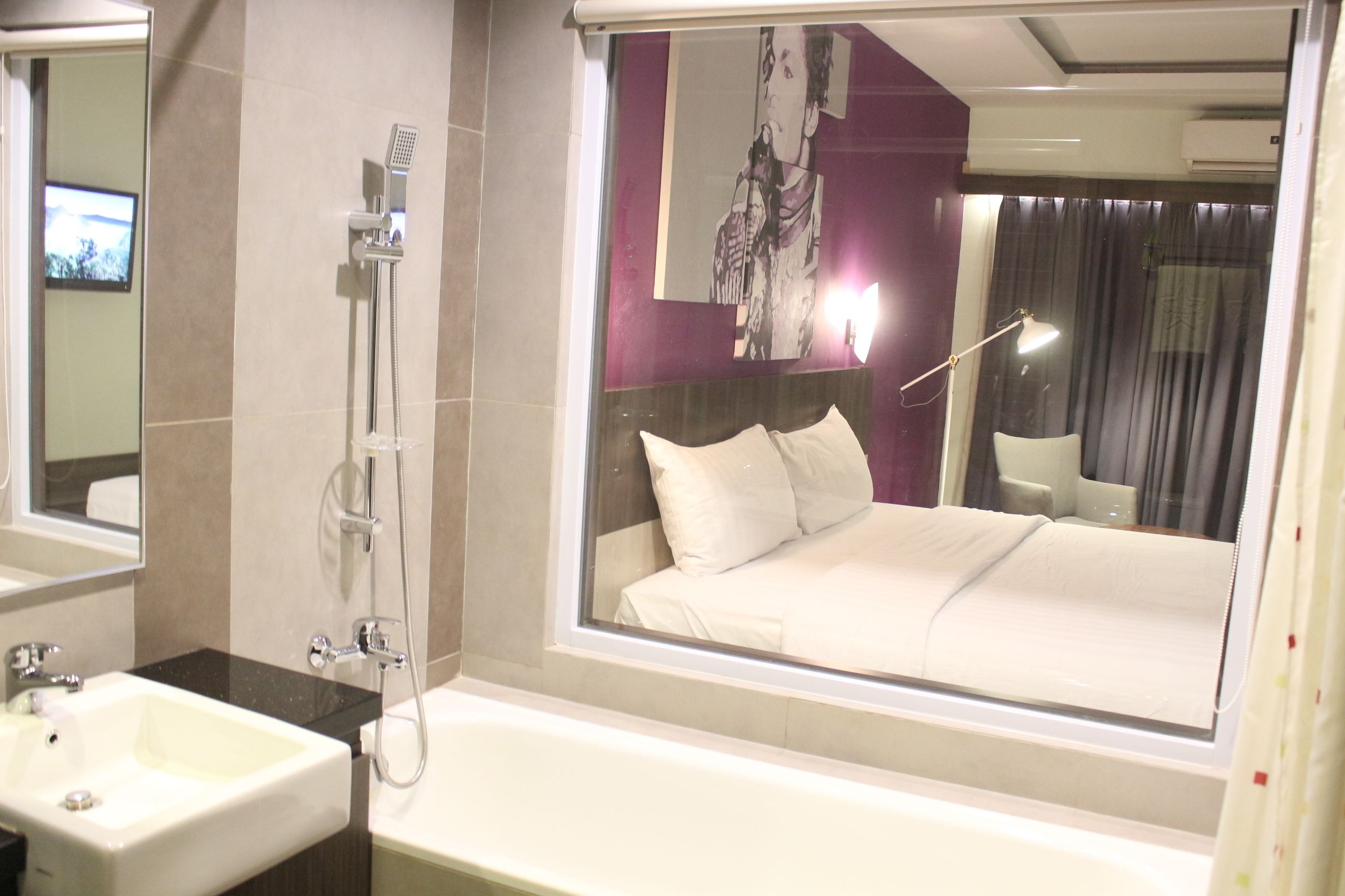 Habitación de hotel con una cama grande, baño con lavamanos y ducha, y un ventanal con vista a la ciudad.