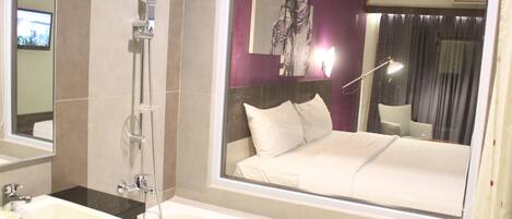 Habitación de hotel con una cama grande, baño con lavamanos y ducha, y un ventanal con vista a la ciudad.