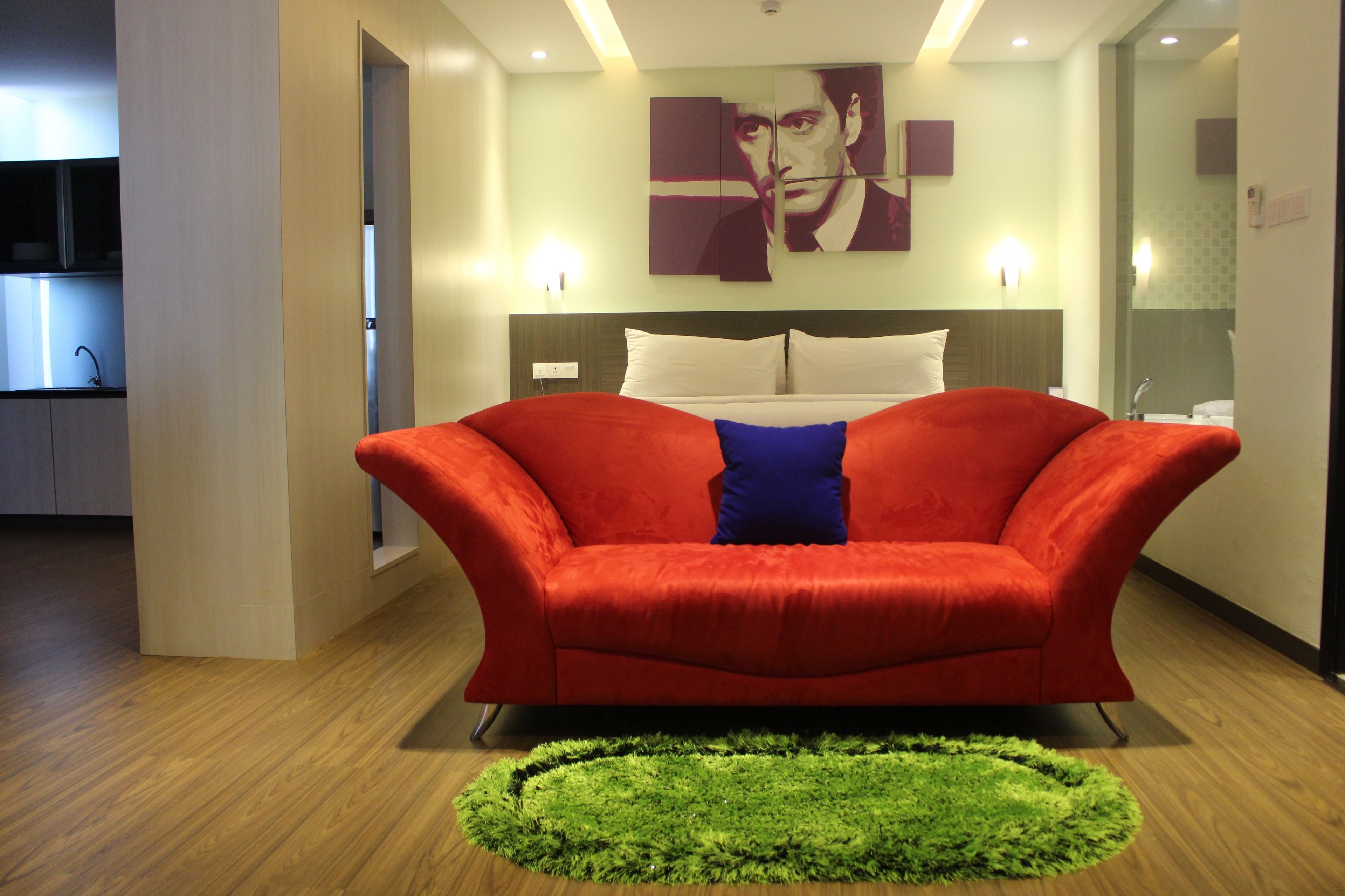 A modern hotel room with a red sofa, a green rug, and a painting on the wall.