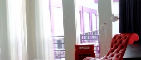Una habitación de hotel con una cama, un sillón rojo, una mesita y un teléfono.