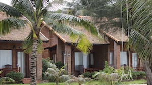 A two-story brick building with a tiled roof, a covered porch, and a garden with palm trees and shrubs. - Gold Coast Phu Quoc Resort (Phu Quoc)