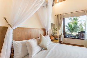 A bed with white linens, a wooden headboard, and a canopy. There is a window with a view of palm trees. - Gold Coast Phu Quoc Resort (Phu Quoc)