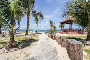 A beach pathway leading to a wooden gazebo with a thatched roof, surrounded by palm trees and beach chairs. - Gold Coast Phu Quoc Resort (Phu Quoc)
