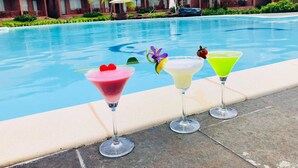 A poolside view with three cocktails, a clear blue pool, and red-roofed buildings in the background. - Gold Coast Phu Quoc Resort (Phu Quoc)