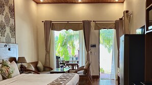 A bedroom with a large bed, wooden flooring, a ceiling with a wooden design, and a view of the outdoors through a window. - Gold Coast Phu Quoc Resort (Phu Quoc)