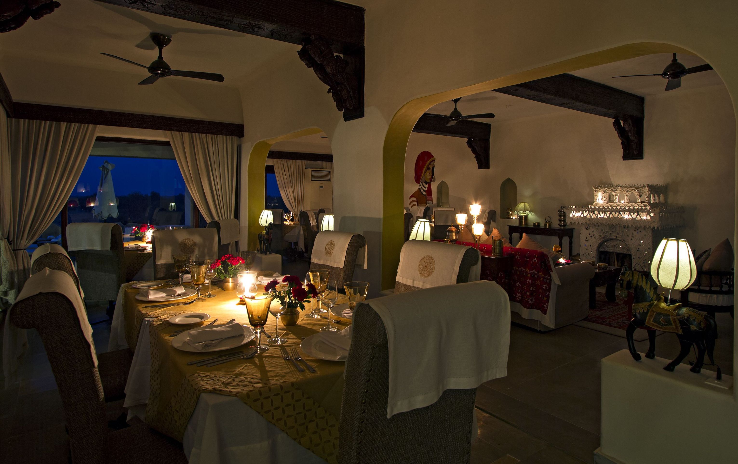 A dimly lit dining area with tables set for a meal, featuring candles and tablecloths.