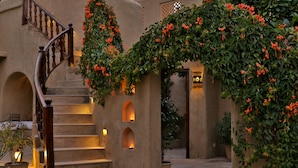 A staircase with a wooden handrail, a potted plant, and a wall with a decorative archway. - Mihir Garh (Rohat)
