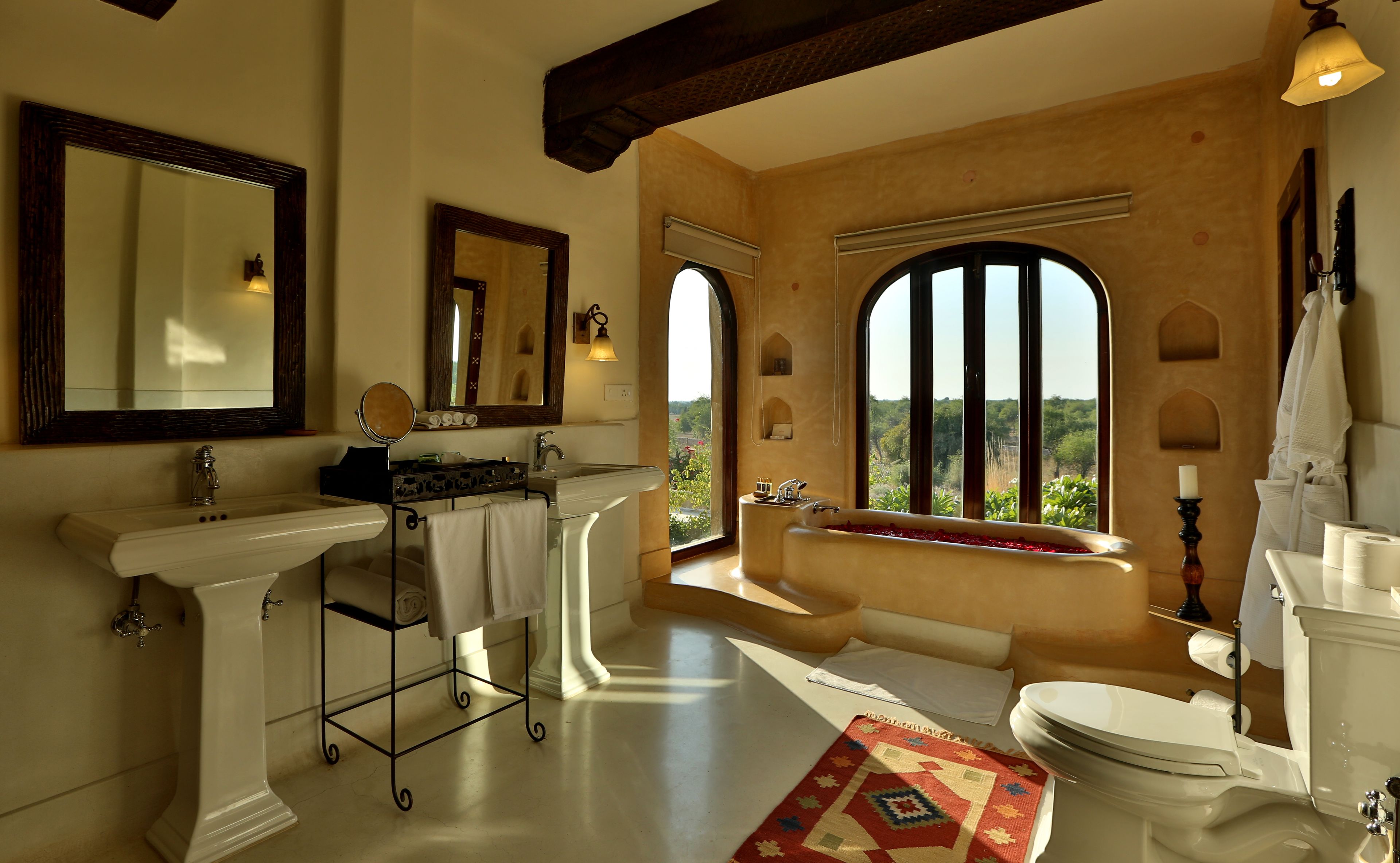 A bathroom with a large mirror, a sink, a bathtub, and a toilet. There is a window with a view of greenery outside.