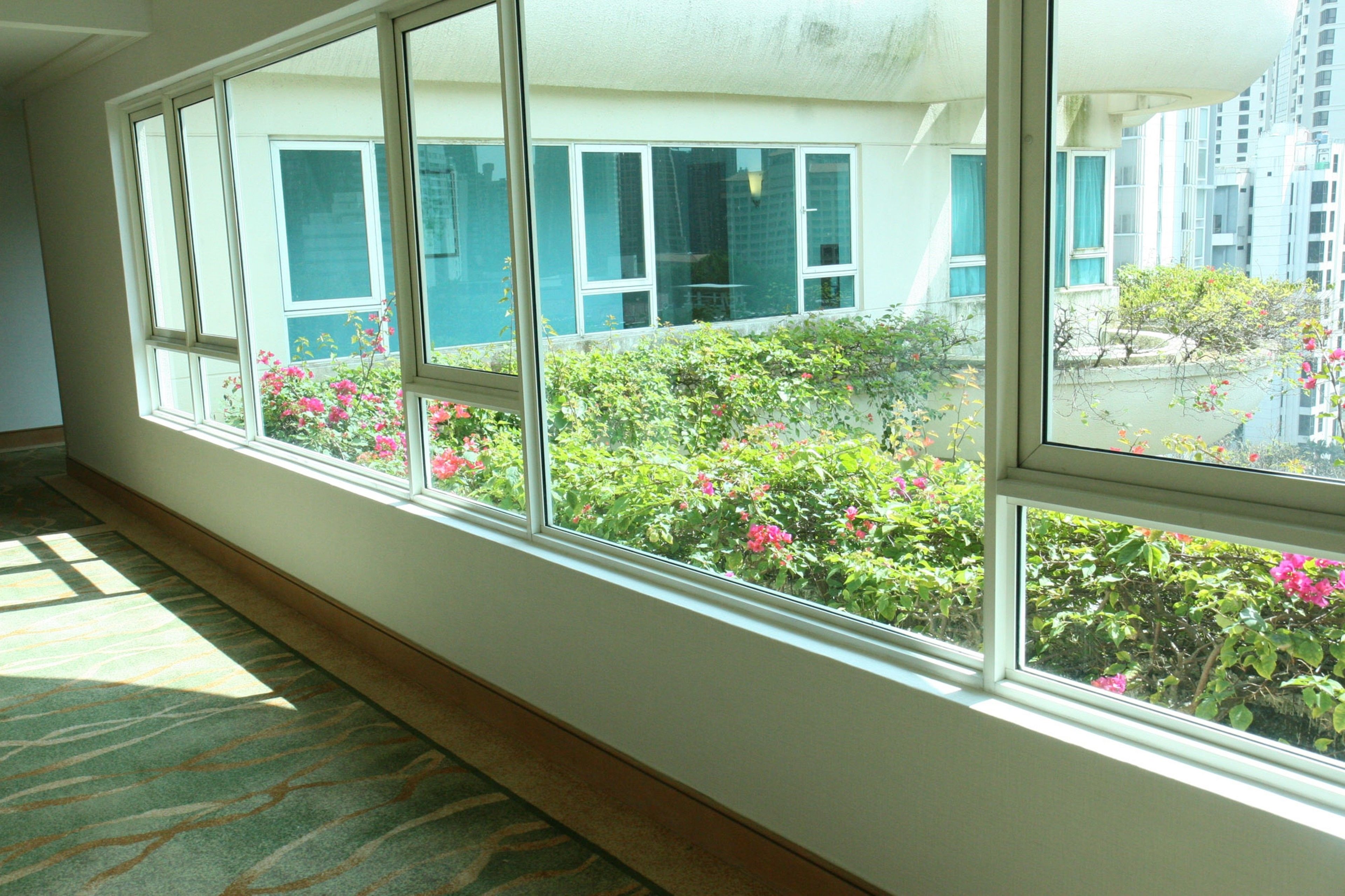 A hotel room with large windows, carpeted floor, and a view of a building with balconies.