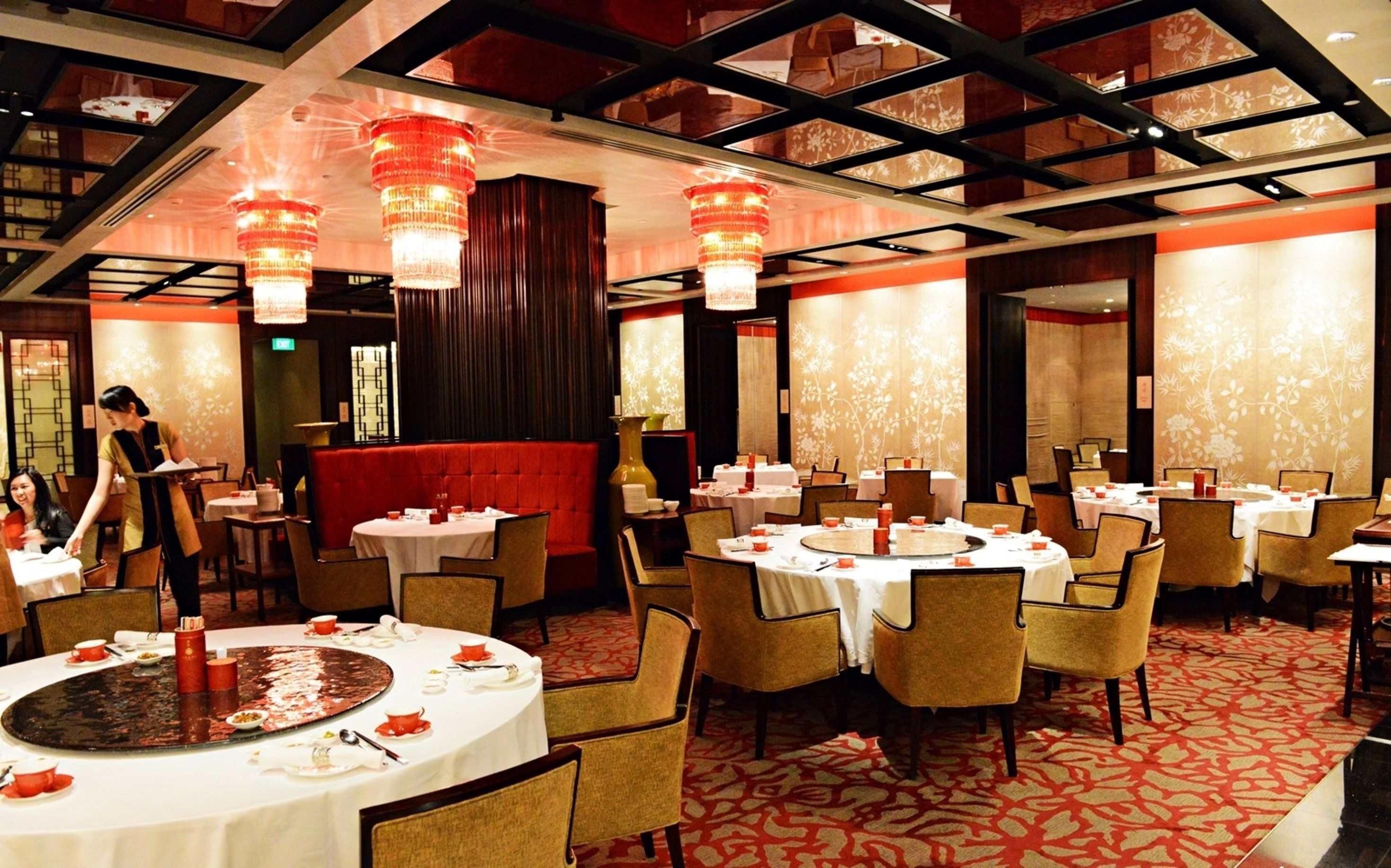 A restaurant with round tables, red upholstered booths, and chandeliers.