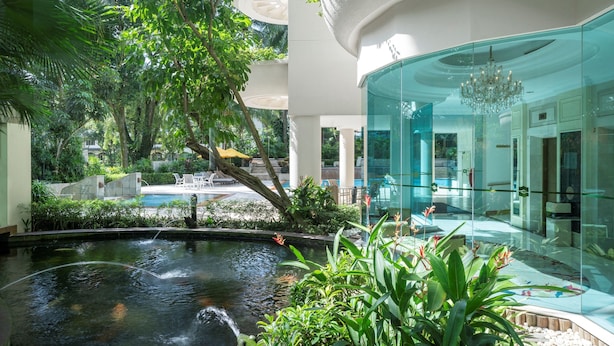 Ein modernes Hotel mit einem zentralen Wasserspiel, üppigem Grün und einem gläsernen Empfangsbereich.