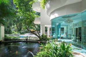 Ein modernes Hotel mit einem zentralen Wasserspiel, üppigem Grün und einem gläsernen Empfangsbereich.