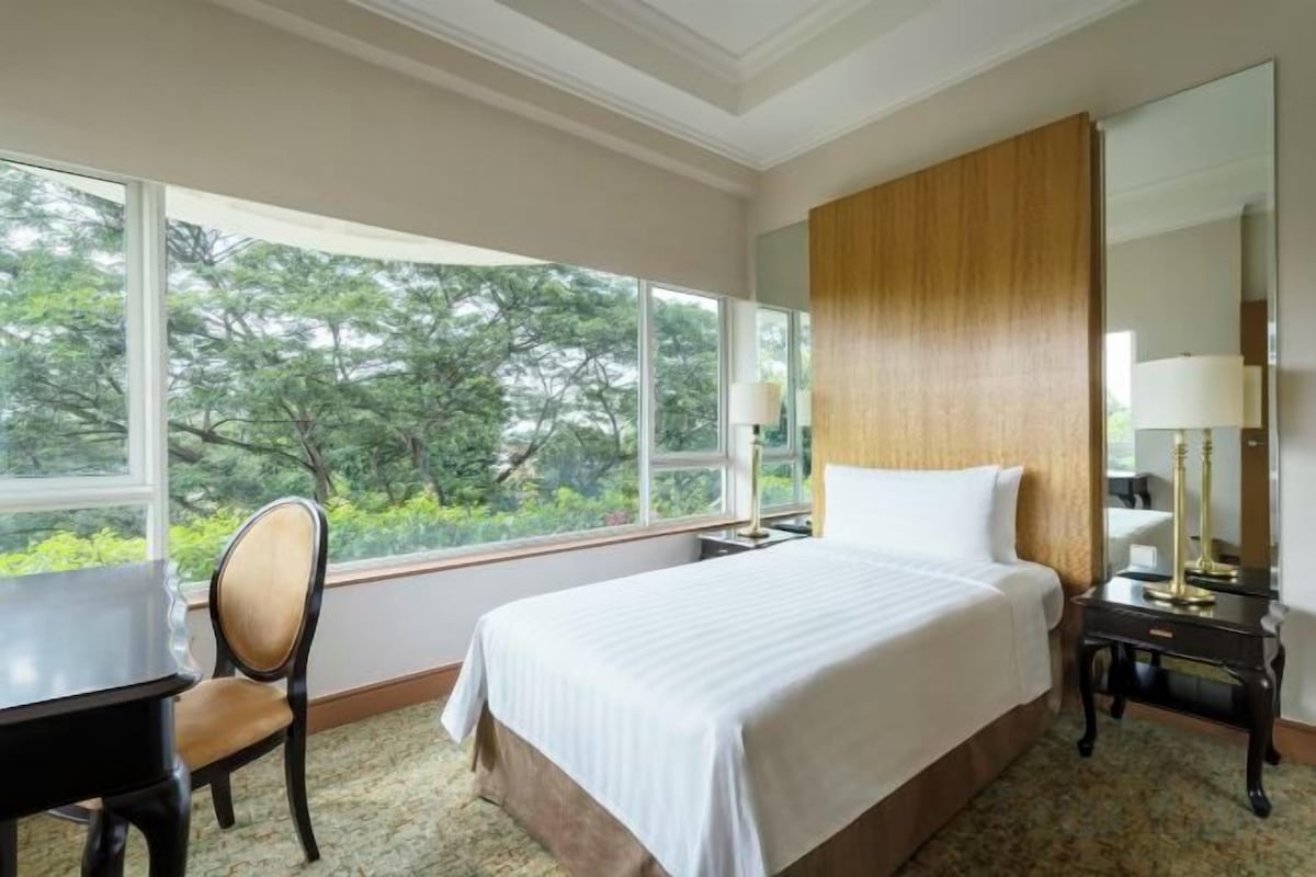 A hotel room with a large bed, a desk, a chair, a nightstand, and a mirror.