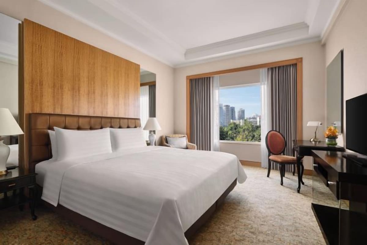 A hotel room with a large bed, a desk, a chair, and a TV.