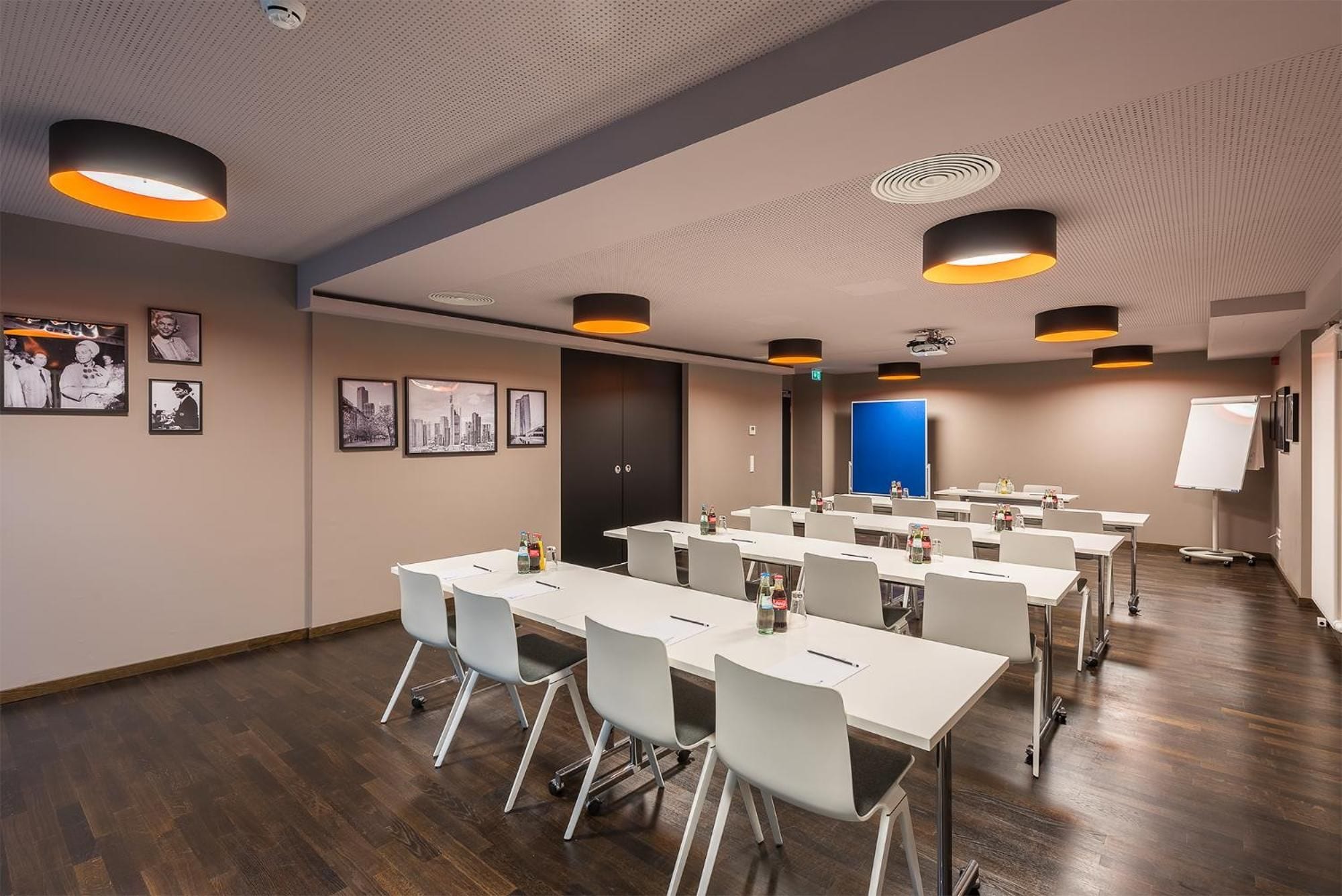 A conference room with white tables and chairs, a blue door, and framed pictures on the wall.