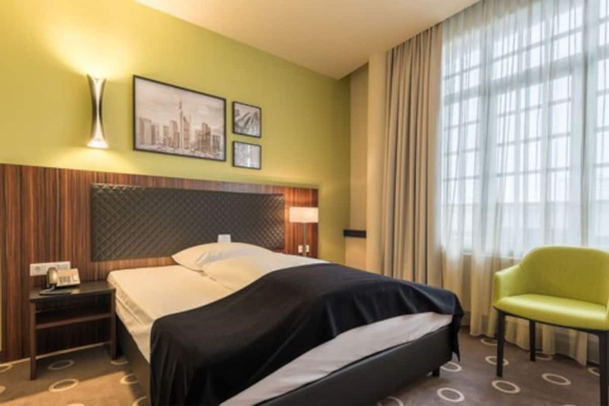 A hotel room with a bed, a nightstand, a lamp, a chair, and a window with curtains.