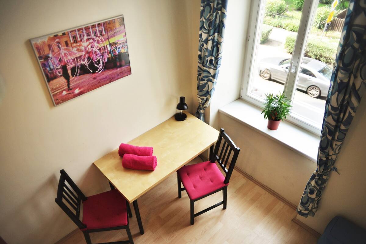Un pequeño comedor con una mesa de madera, dos sillas y una planta en maceta junto a la ventana.