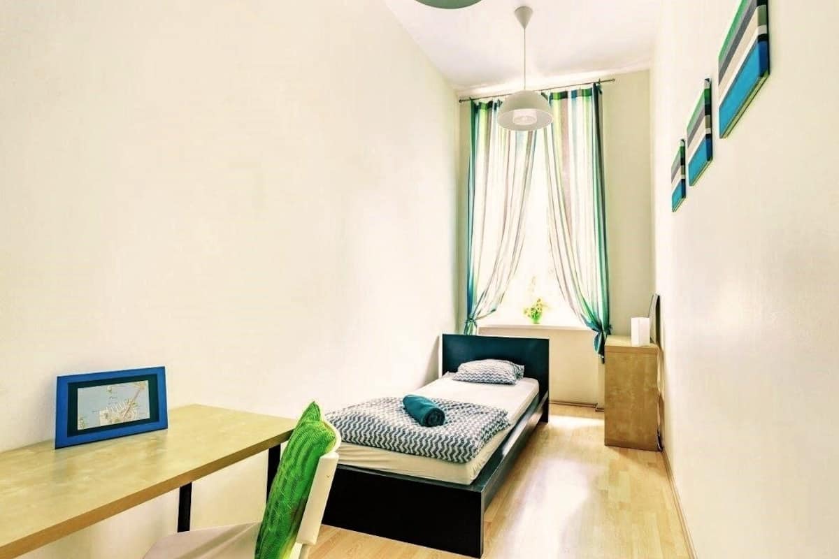 Un dormitorio pequeño y bien iluminado con cama, escritorio y ventana con cortinas.
