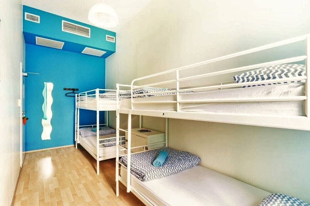 Dormitorio con literas, tres camas dobles, una pared de acento azul, suelo de madera y una mesita de noche con lámpara.