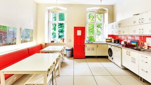 A bright kitchen with a red refrigerator, white cabinets, and a window overlooking greenery. - Grampa's Hostel (Wroclaw)