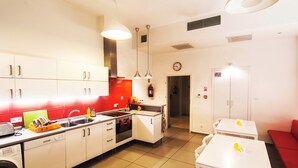 A modern kitchen with white cabinets, a red backsplash, and a dining area with a red sofa. - Grampa's Hostel (Wroclaw)