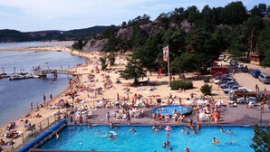 A beach with a swimming pool, beach chairs, and umbrellas.