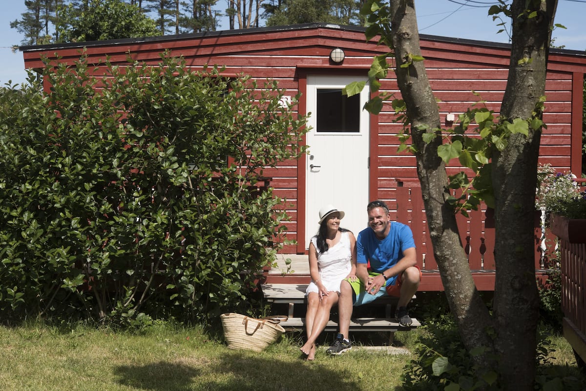 Un couple est assis sur un banc devant un bâtiment en bois rouge dont la porte est blanche.