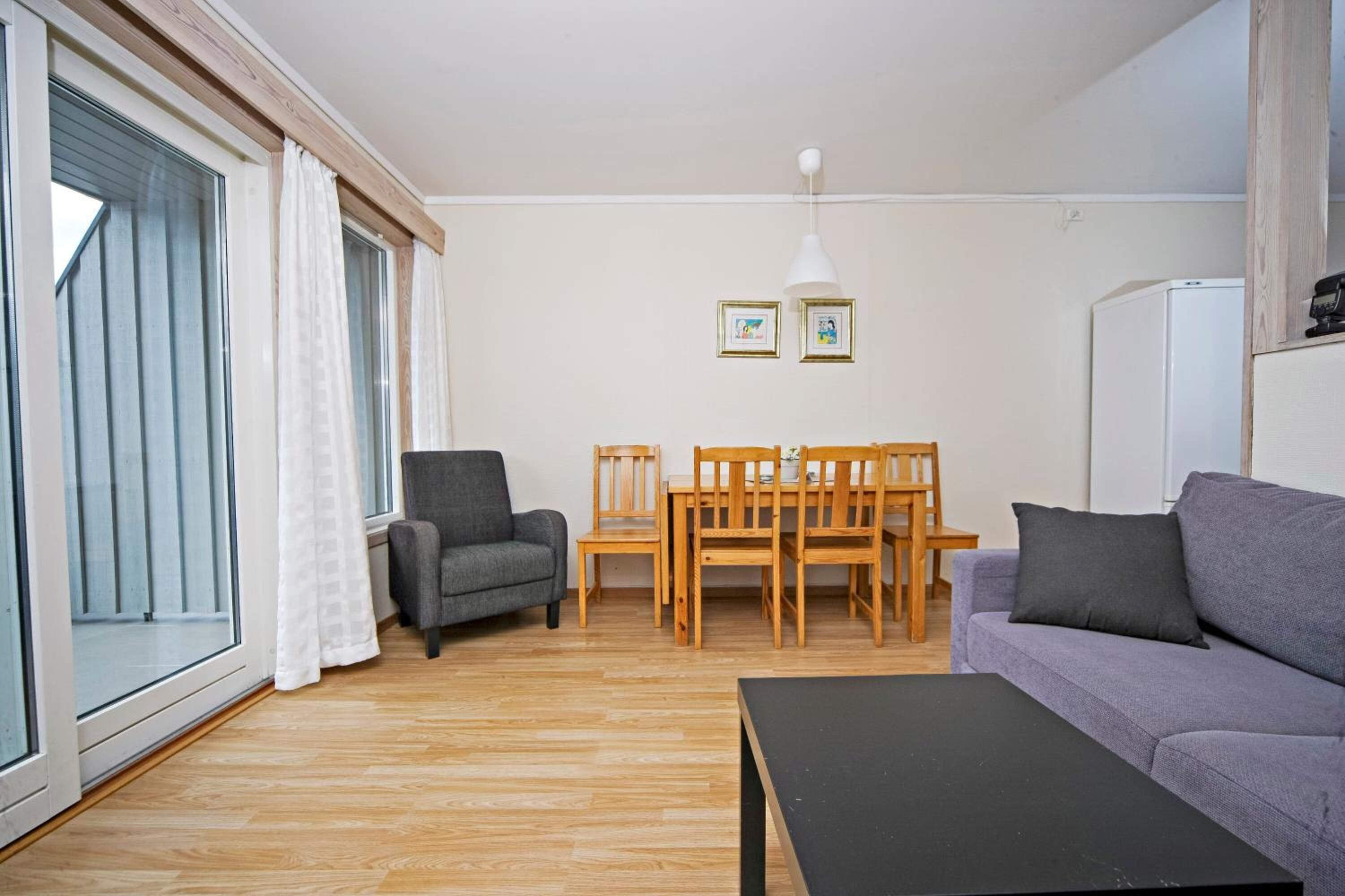 A living room with a sofa, a table, a chair, a dining table with chairs, and a refrigerator.