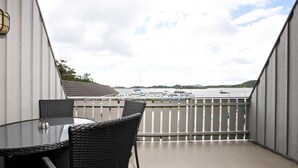 A balcony with a round table and chairs, offering a view of boats on water.