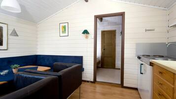 Habitació compacta amb un sofà blau, una taula de menjador de fusta, una cuineta amb fogó i una porta que condueix a una altra habitació.