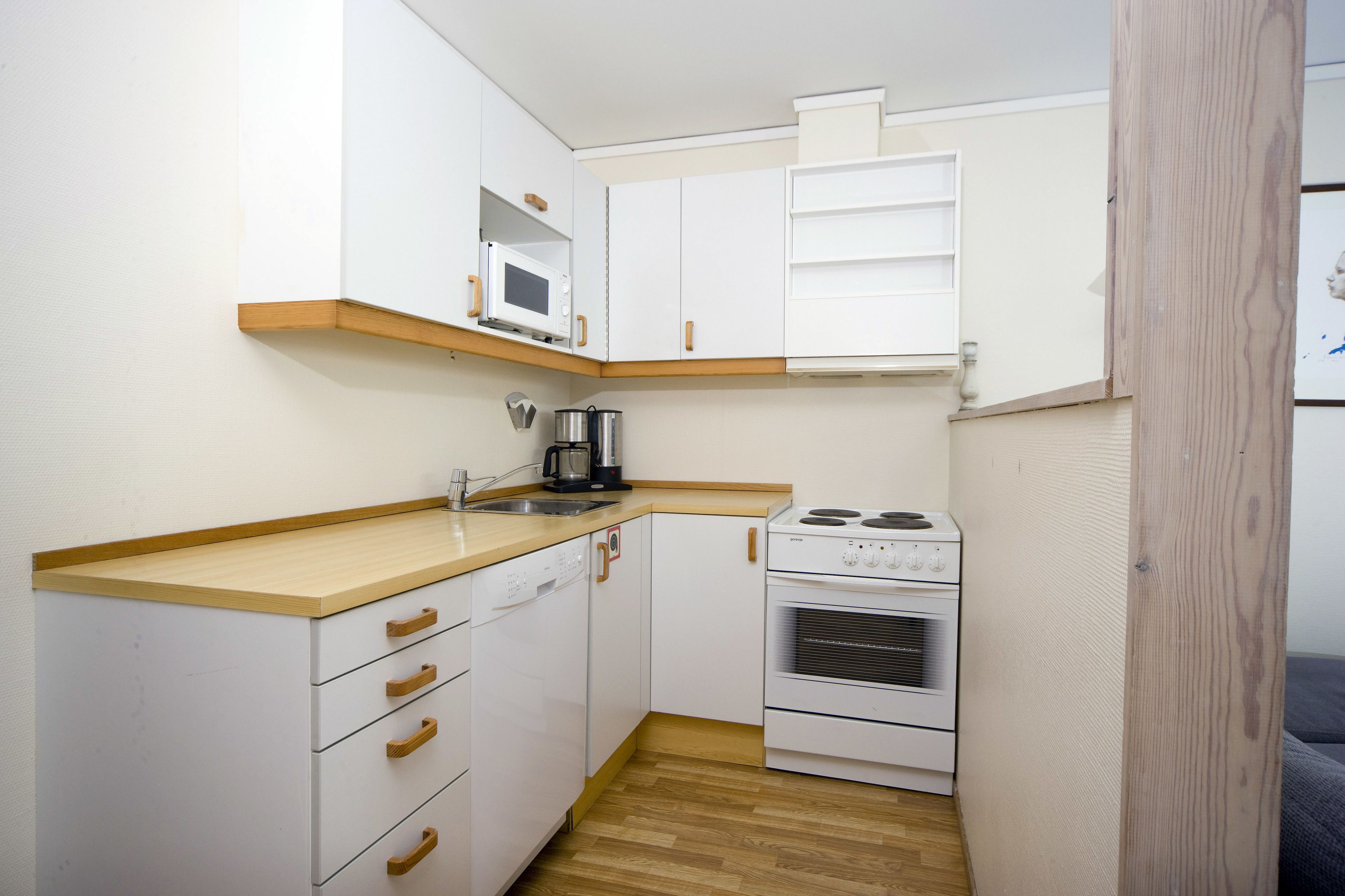 Una cocina compacta con armarios blancos, un microondas, una cafetera y una estufa.