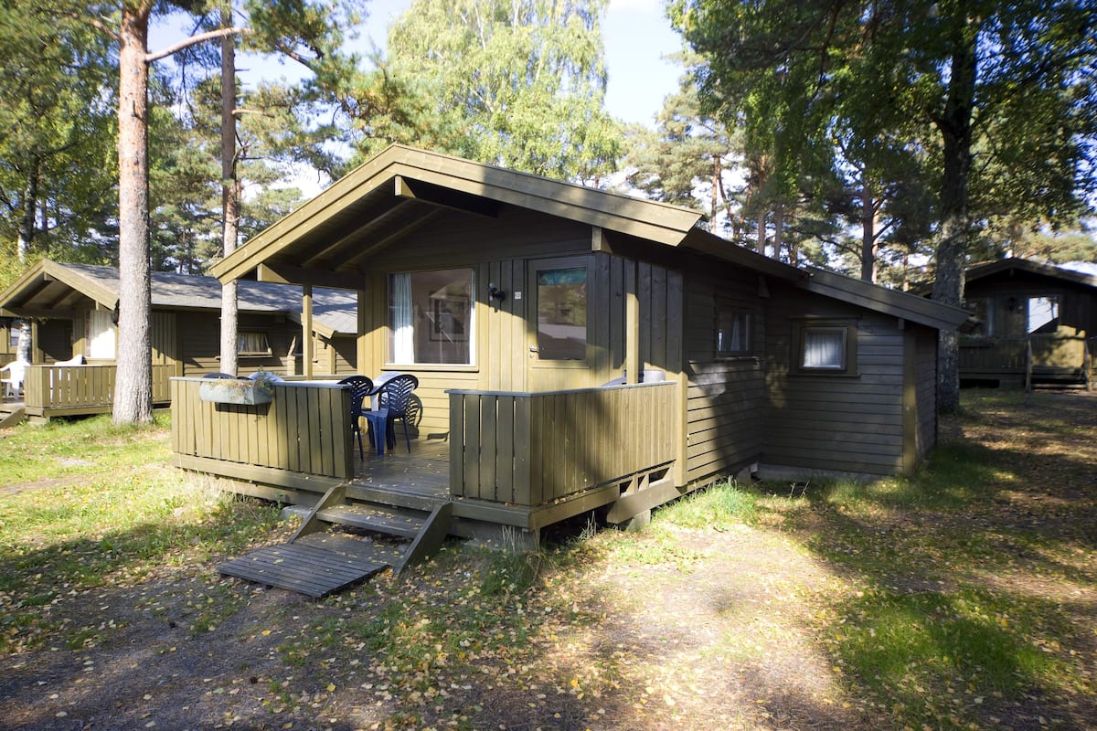 Une cabane en bois avec une véranda, une petite terrasse et une fenêtre.