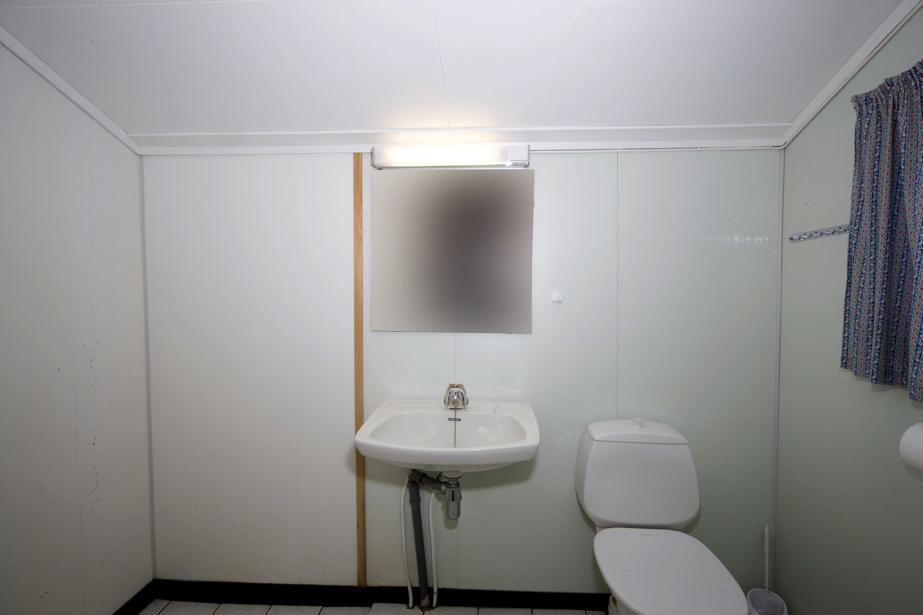 Ett litet, enkelt badrum med ett vitt handfat, en toalett och en spegel ovanför handfatet.