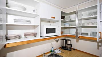 Une cuisine compacte avec des meubles blancs, un four à micro-ondes, une machine à café et un évier.