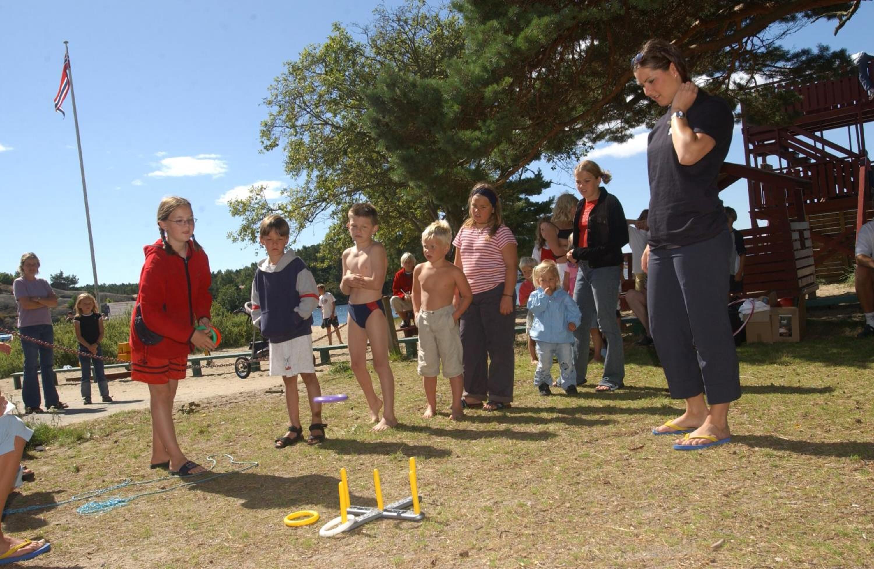 A group of people outdoors, some standing and some sitting, with a playground structure in the background.