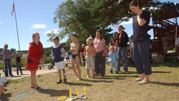 A group of people outdoors, some standing and some sitting, with a playground structure in the background.