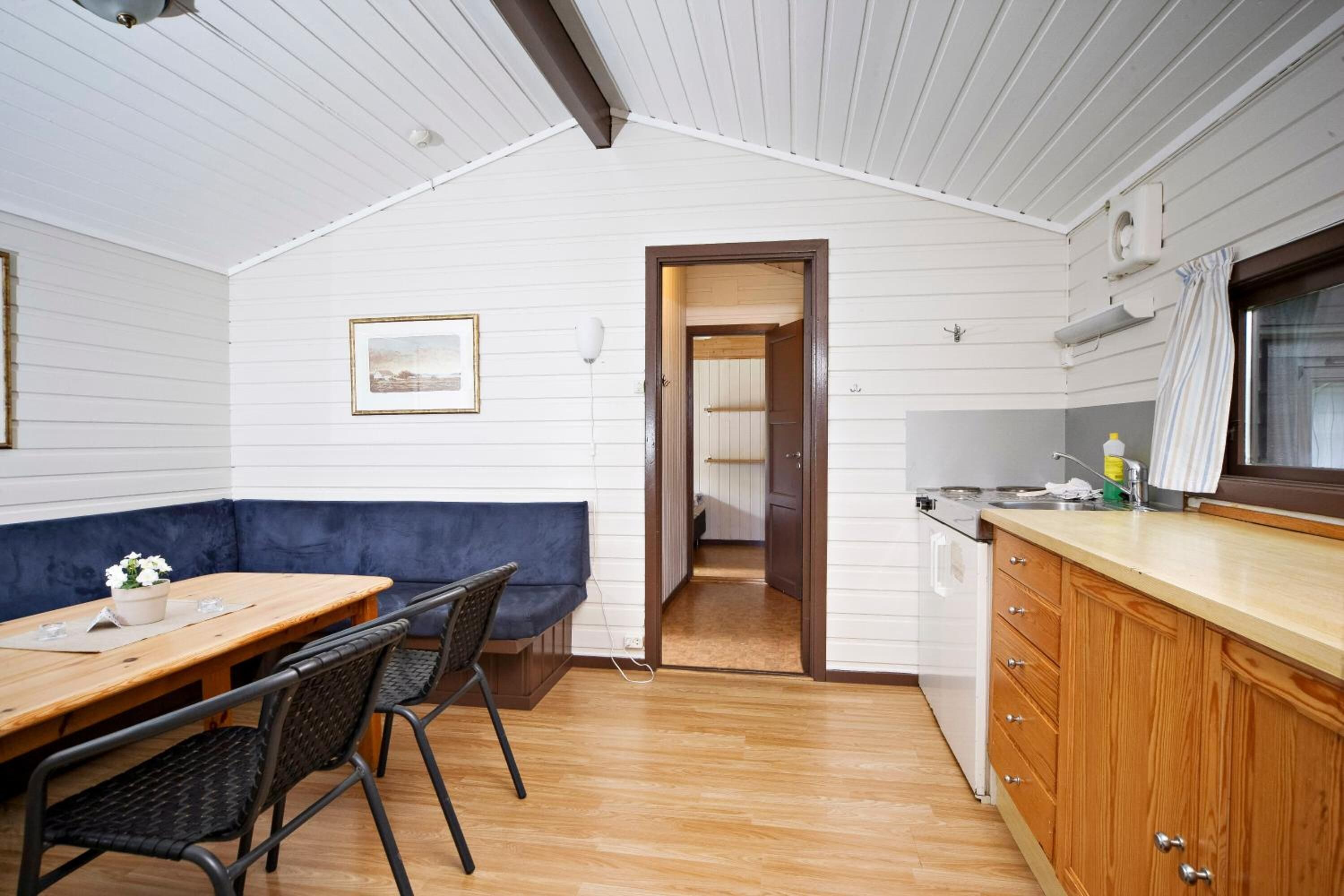 Una cocina compacta con armarios de madera, una zona de comedor con un banco azul y una puerta visible que da a otra habitación.