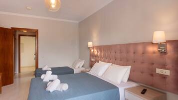 A hotel room with two beds, a wooden door, a bedside table with a lamp, and a wall-mounted light fixture.