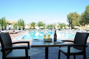 A poolside area with lounge chairs and umbrellas, a table with drinks and a plate, and a clear view of the pool. - Alkion Hotel Sidari (Corfu)