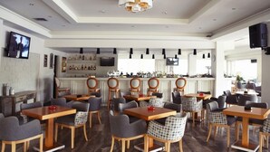 A modern restaurant with wooden tables and chairs, a bar area with bottles, and a television screen. - Alkion Hotel Sidari (Corfu)