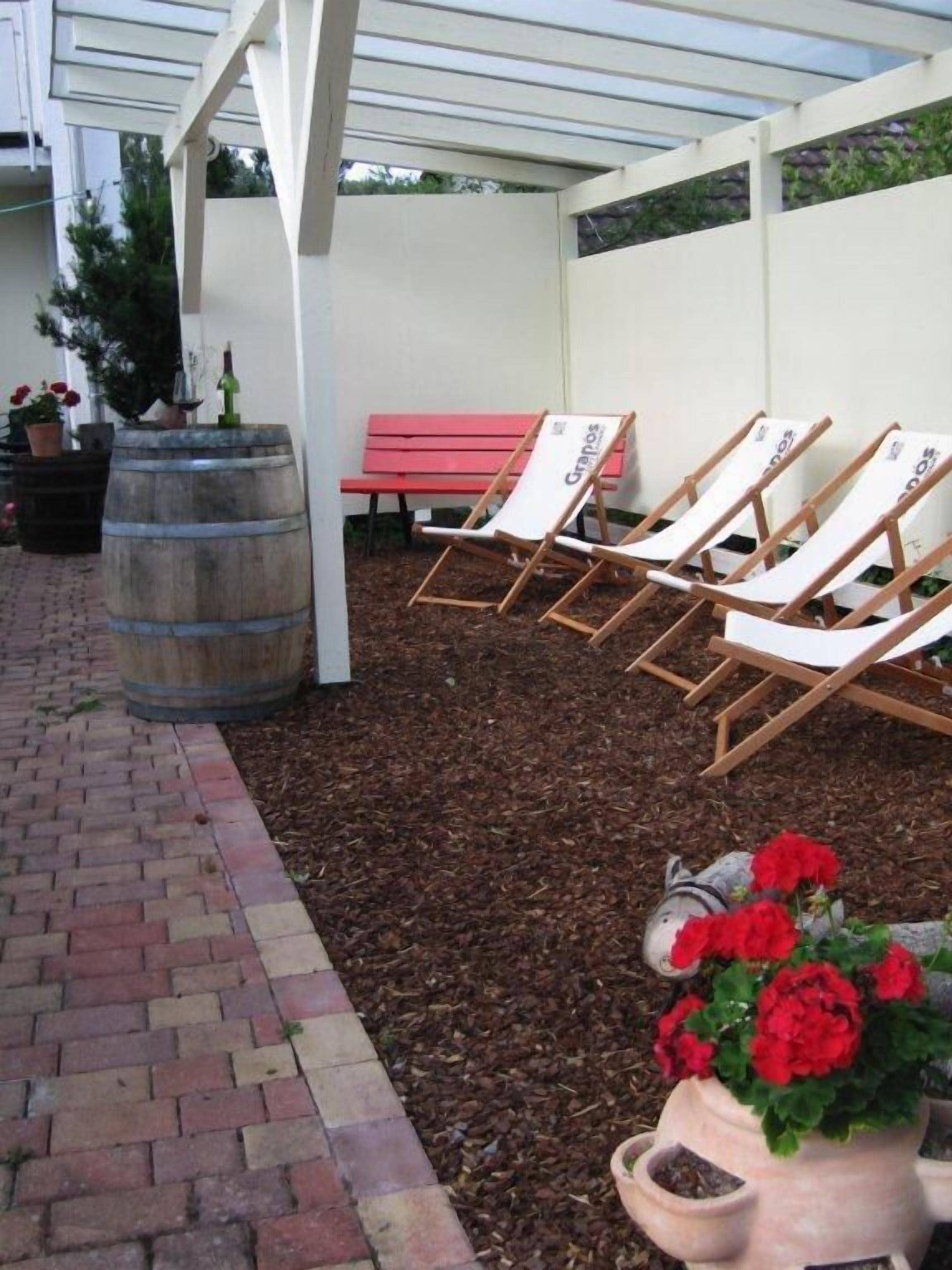 An outdoor seating area with wooden lounge chairs and a red bench under a white pergola.