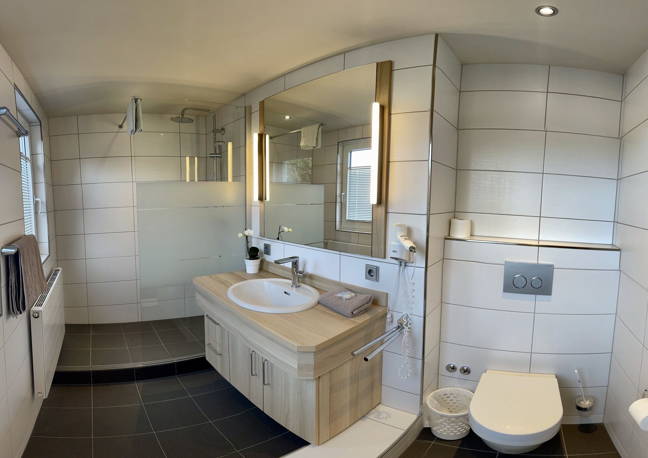 A modern bathroom with a large mirror, a sink, a shower, and a toilet.