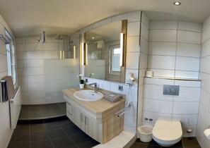 A modern bathroom with a large mirror, a sink, a shower, and a toilet. - Landhotel zur Linde (Lossburg)