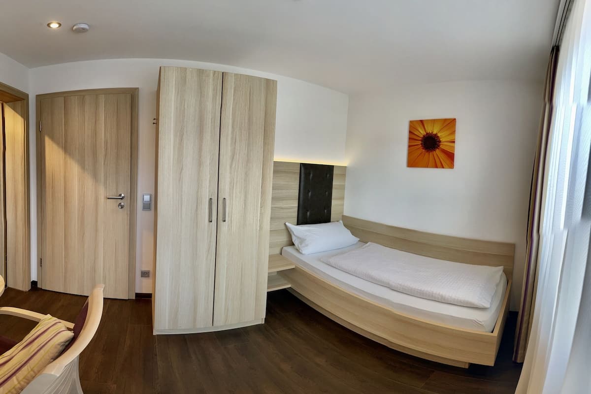 A modern bedroom with a curved bed, wooden wardrobe, and a single wall-mounted artwork.
