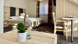 A modern hotel room with a bed, bedside table, chair, desk, and a potted plant. - Landhotel zur Linde (Lossburg)
